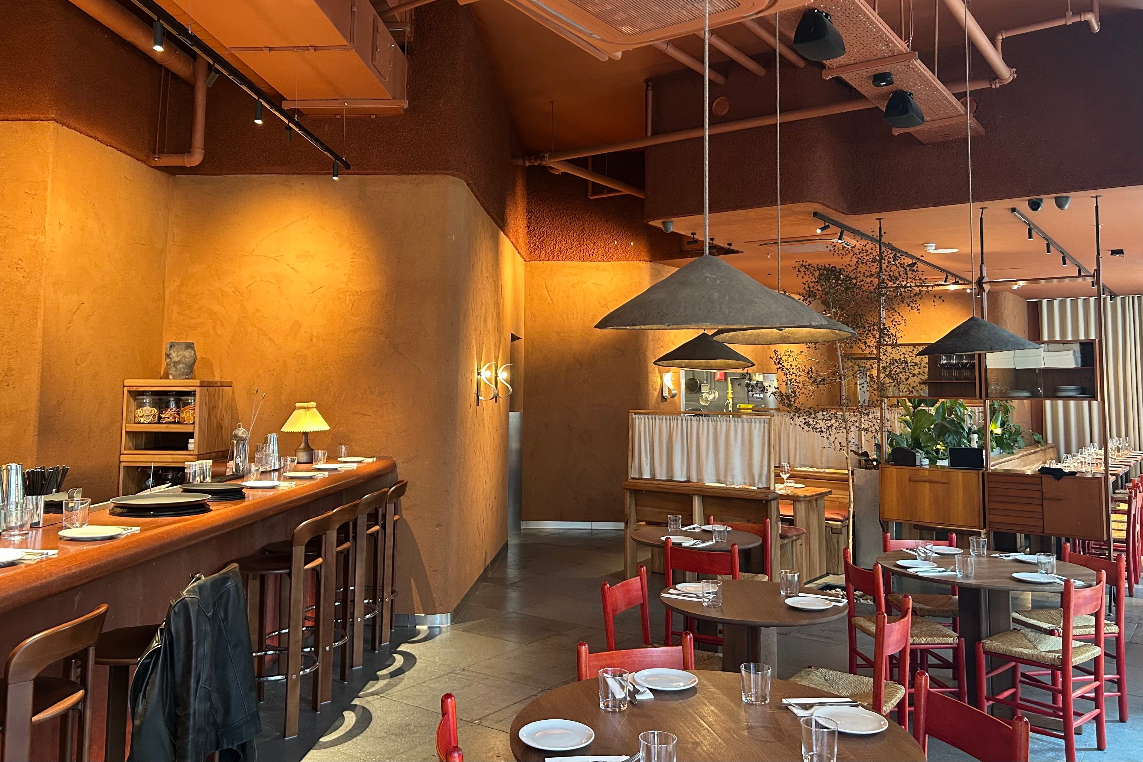 A dimly lit interior of Ara restaurant with red chairs and orange walls